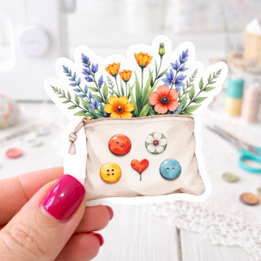 Sticker featuring a Small pouch with floral design and colorful buttons held by a hand on a blurred craft background