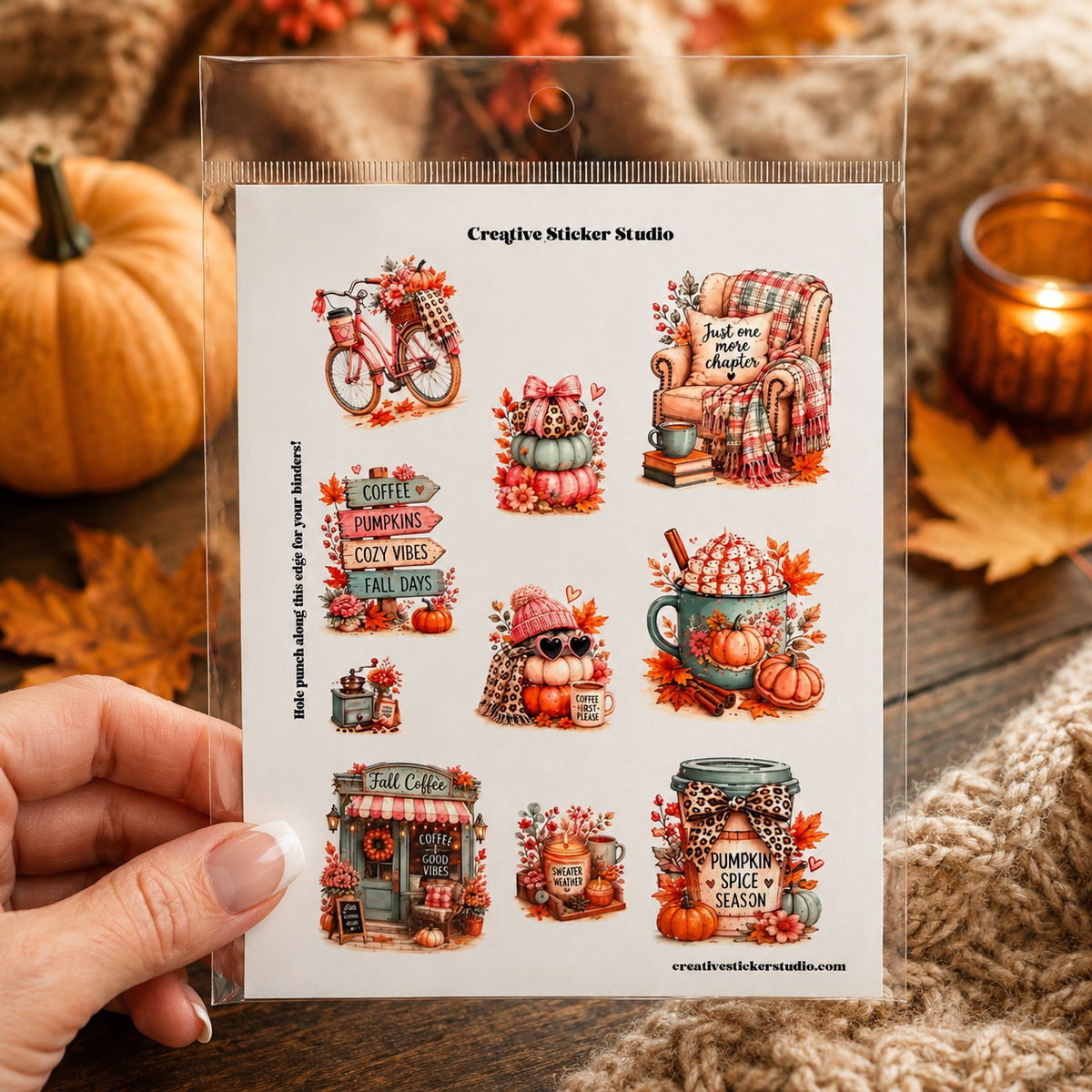 A hand holds a clear plastic package containing a sheet of autumn-themed stickers from Creative Sticker Studio. The stickers feature cozy fall illustrations including a bicycle, pumpkins, a rocking chair, a coffee shop, a mug with a cinnamon stick, and a spice jar, all in warm autumn colors.