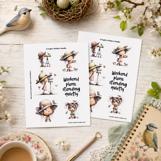Two printed sticker sheets from Craigie Nicker Studio featuring cute illustrated characters and the text 'Weekend plans: standing quietly,' arranged on a light wood surface with a bird, eggs, flowers, a cup, and a notebook nearby.