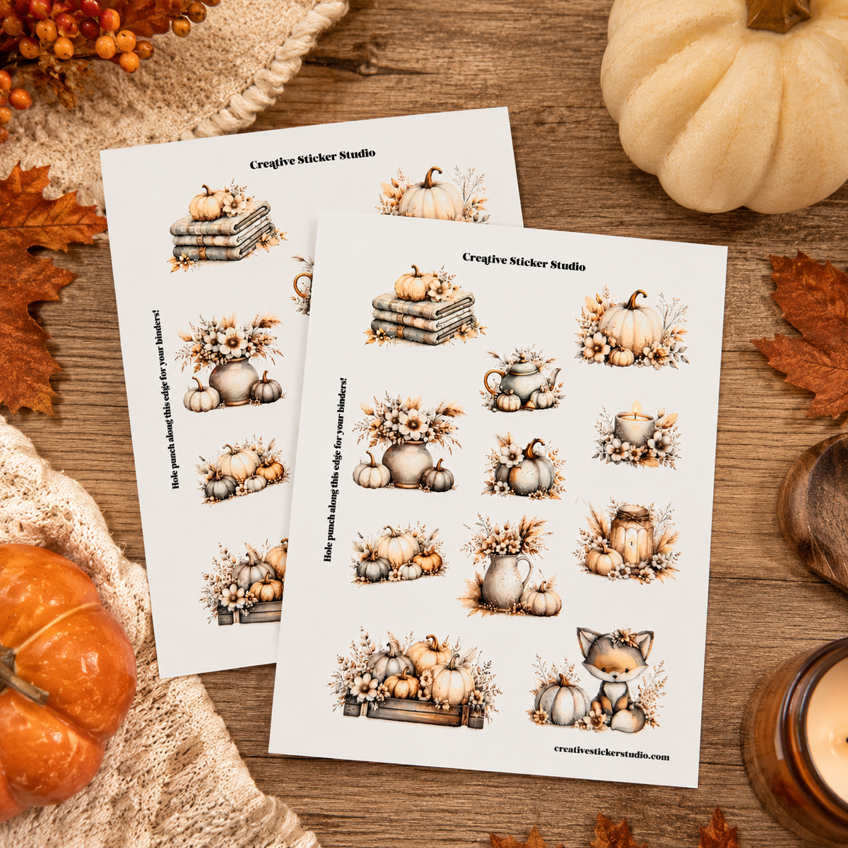 Two printed sticker sheets titled 'Creative Sticker Studio' displayed on a rustic wooden surface with autumn props including pumpkins, leaves, and a candle. The sheets feature illustrated pumpkins, gourds, books, and a fox in muted beige, brown, and gray tones.