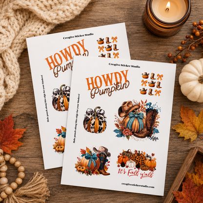 Two printed sticker sheets with autumn-themed designs titled 'Howdy Pumpkin' are arranged on a wooden surface with a knitted blanket, candle, small pumpkin, fall leaves, and beads around them. The sheets show illustrated pumpkins, acorns, leaves, and fall motifs in orange, brown, blue, and cream tones.