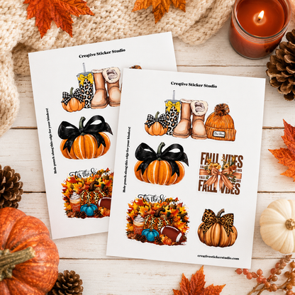 Two printed sticker sheets displayed on a rustic white wood surface with autumn props including pumpkins, pinecones, fall leaves, a knitted scarf, and a lit candle. The sheets feature illustrated fall-themed stickers such as boots with leopard print, pumpkins, bows, autumn leaves, and text reading 'Creative Sticker Studio'.