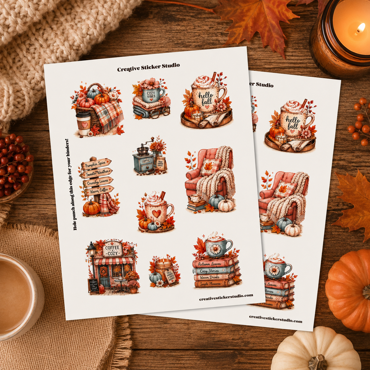 Two printed sticker sheets with autumn-themed illustrations, including mugs, pumpkins, fall leaves, and cozy decor, arranged on a wooden surface with seasonal props like a candle, knit fabric, and small pumpkins.