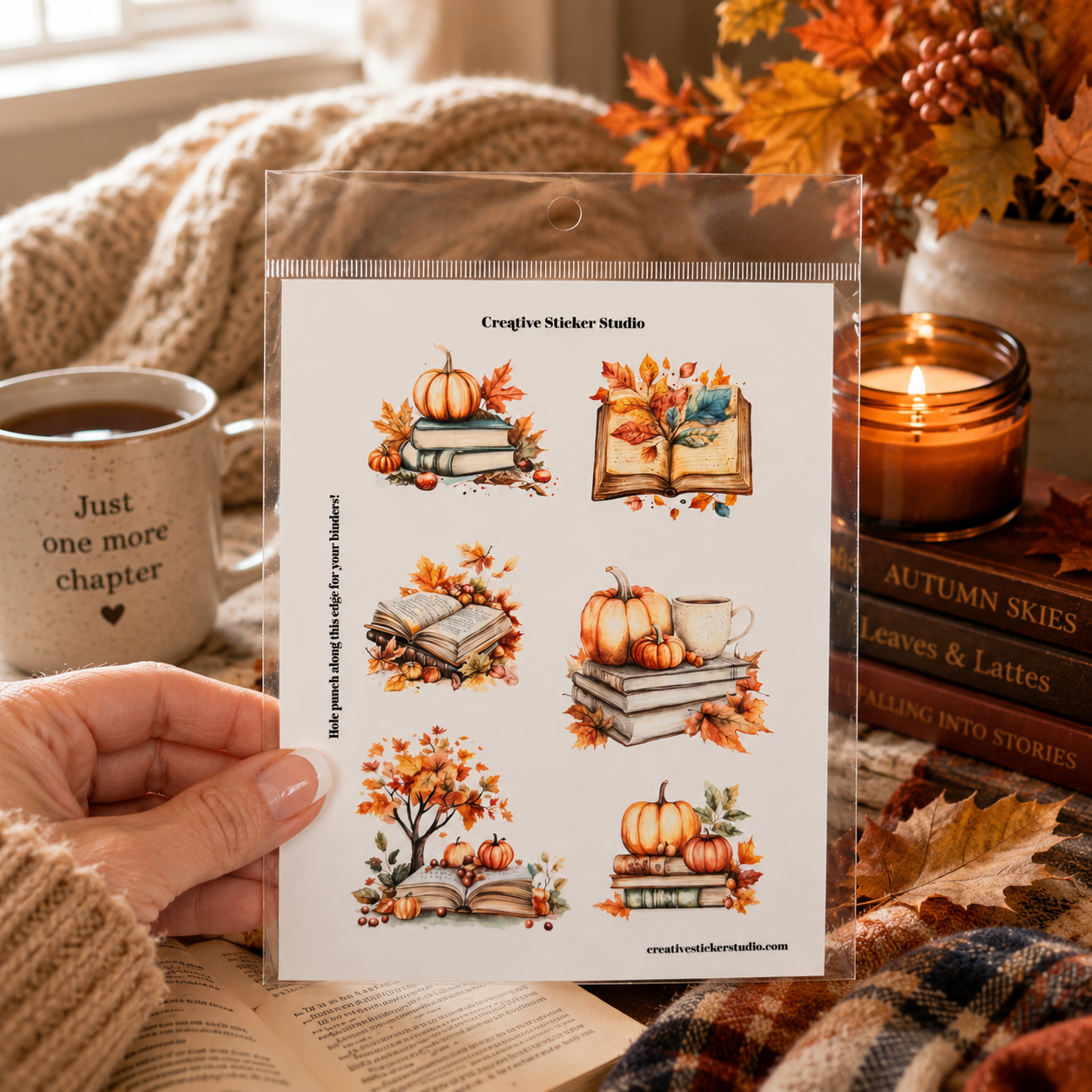 A hand holds a clear plastic sleeve containing a sheet of six autumn-themed sticker designs from Creaghe Sticker Studio. The stickers feature watercolor illustrations of pumpkins, books, and fall foliage.