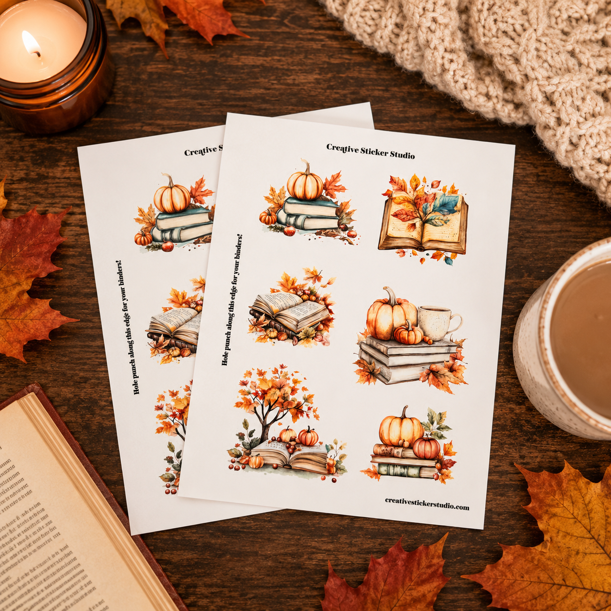 Two printed sticker sheets with autumn-themed illustrations of pumpkins, books, and leaves, styled on a wooden table with fall leaves, a candle, a mug, and a knit blanket.