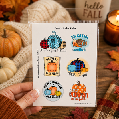 A hand holds a clear plastic sleeve containing a sheet of six autumn-themed sticker designs. The stickers feature colorful pumpkins, plaid patterns, and fall quotes like 'Sweater weather' and 'Happy fall yet!'.