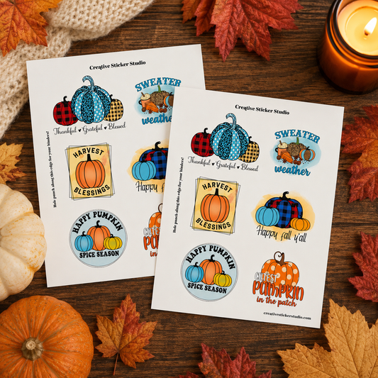 Two printed sticker sheets with autumn-themed illustrations are arranged on a wooden surface with fall leaves, pumpkins, and a lit candle. The stickers include pumpkins, plaid patterns, harvest signs, and seasonal text such as 'Sweater weather' and 'Happy fall yall.