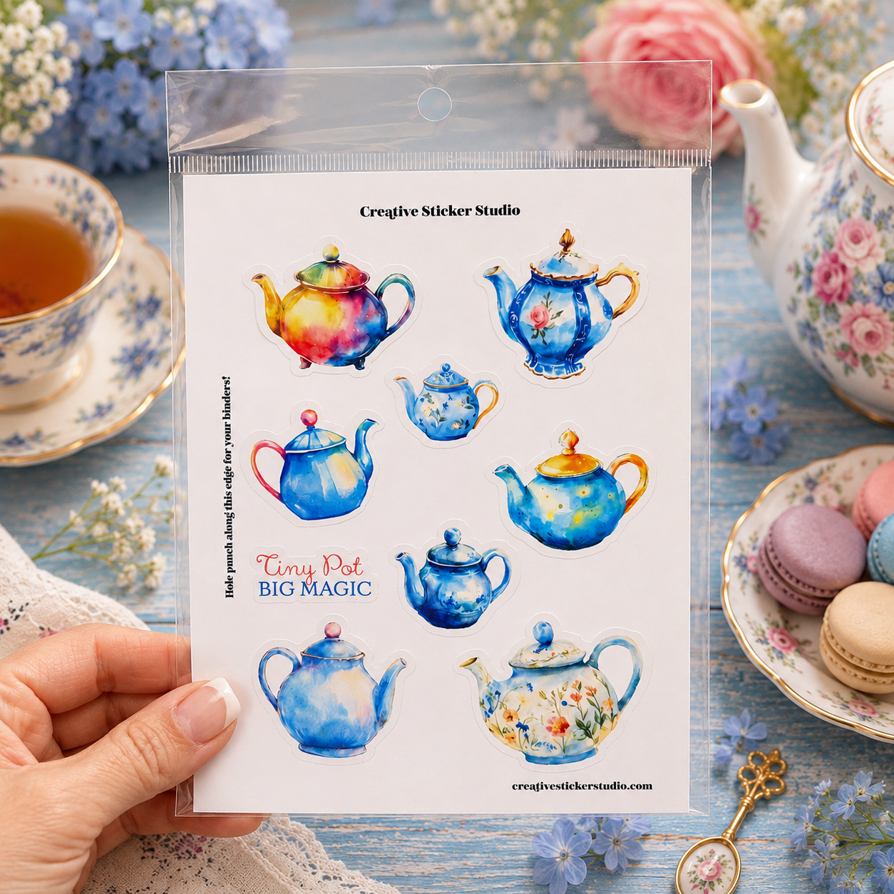 A hand holds a clear plastic bag containing a sheet of watercolor tea pot stickers. The sheet shows multiple colorful teapot designs on a white background with the text 'Creative Sticker Studio' and 'Tiny Pot BIG MAGIC'.