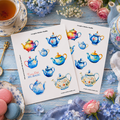 Two printed sheets featuring colorful watercolor illustrations of teapots, arranged on a rustic blue wooden table with tea, flowers, macarons, and a teapot nearby. The sheets read 'Creative Micker Studio' and 'Tea Time Pot BIG MAGIC'.